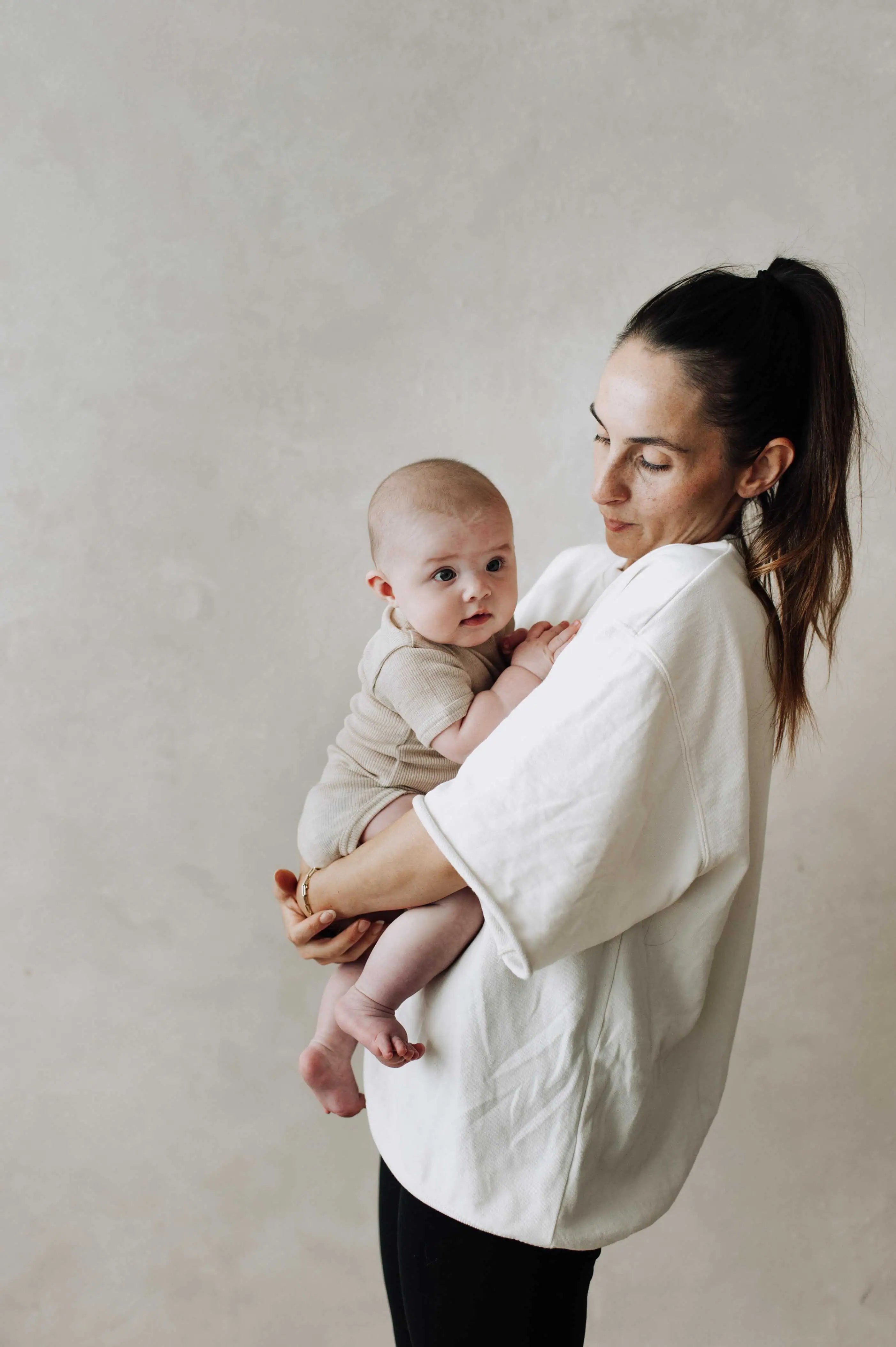 Baby met een wollen romper met korte mouwen die opgetild wordt door zijn moeder