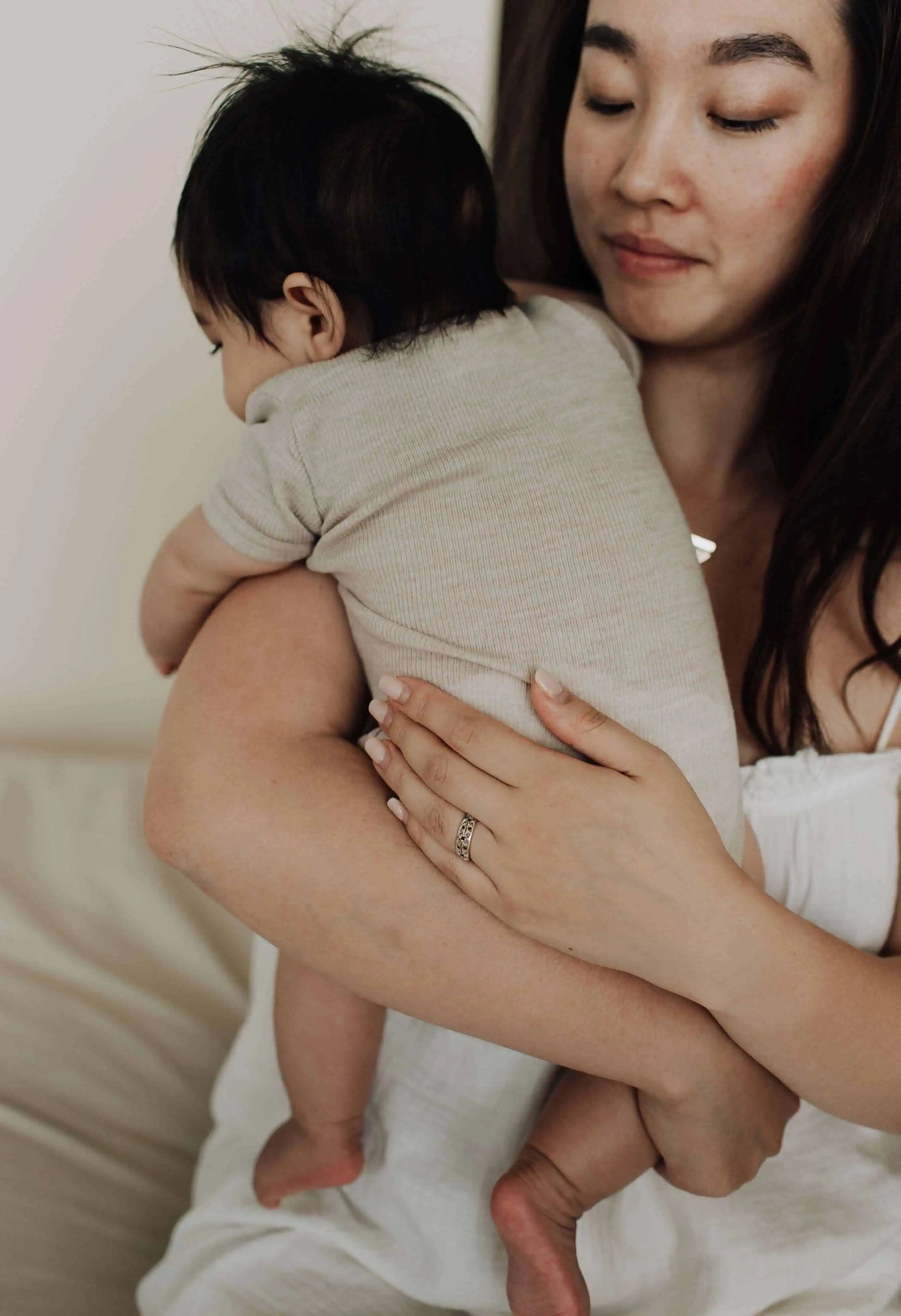 Aziatische moeder met baby met zwart haar over de schouder in romper