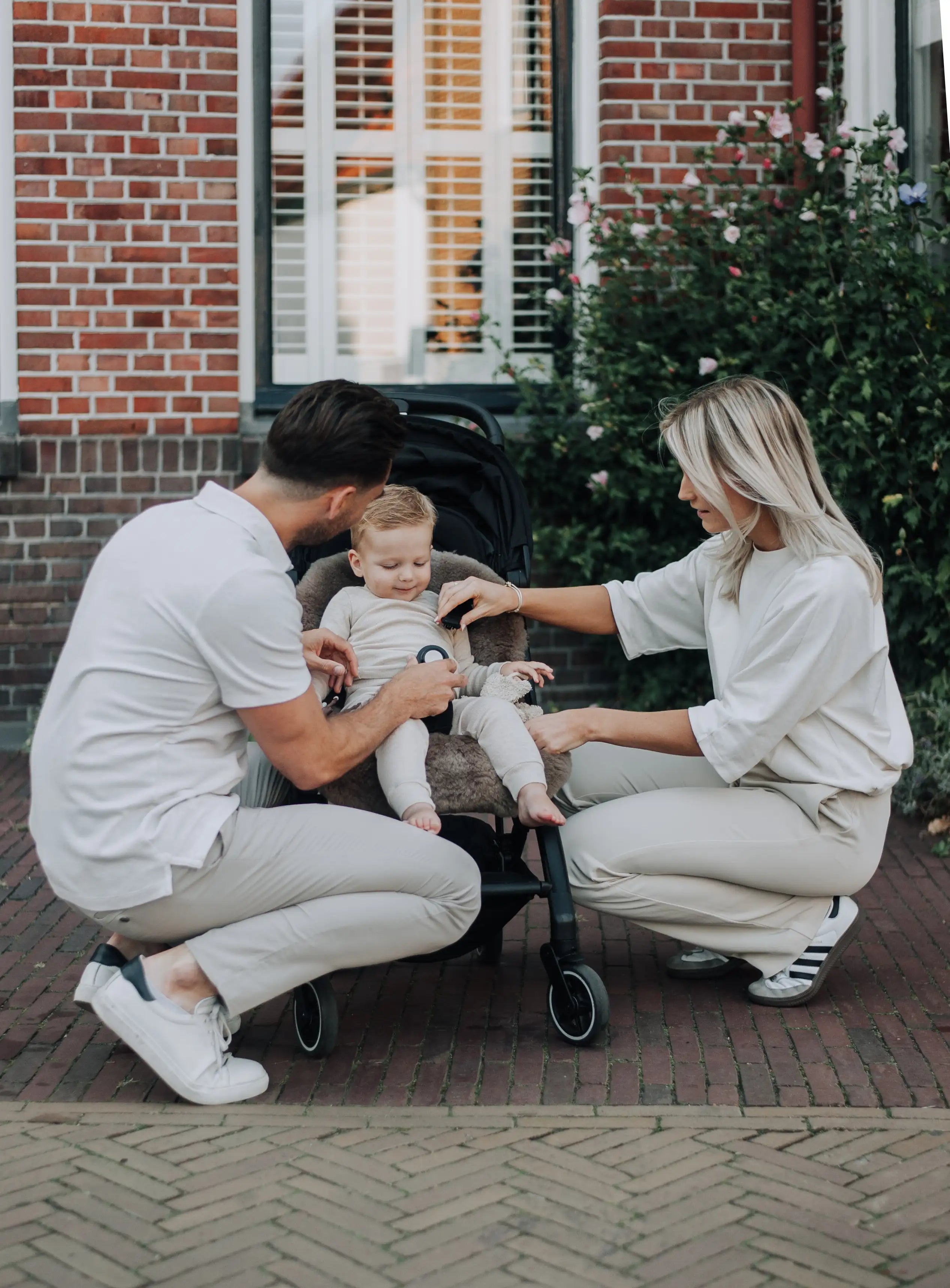 vader en moeder gehurt bij een kind in een kinderwagen die zit op een wollen schapenvacht