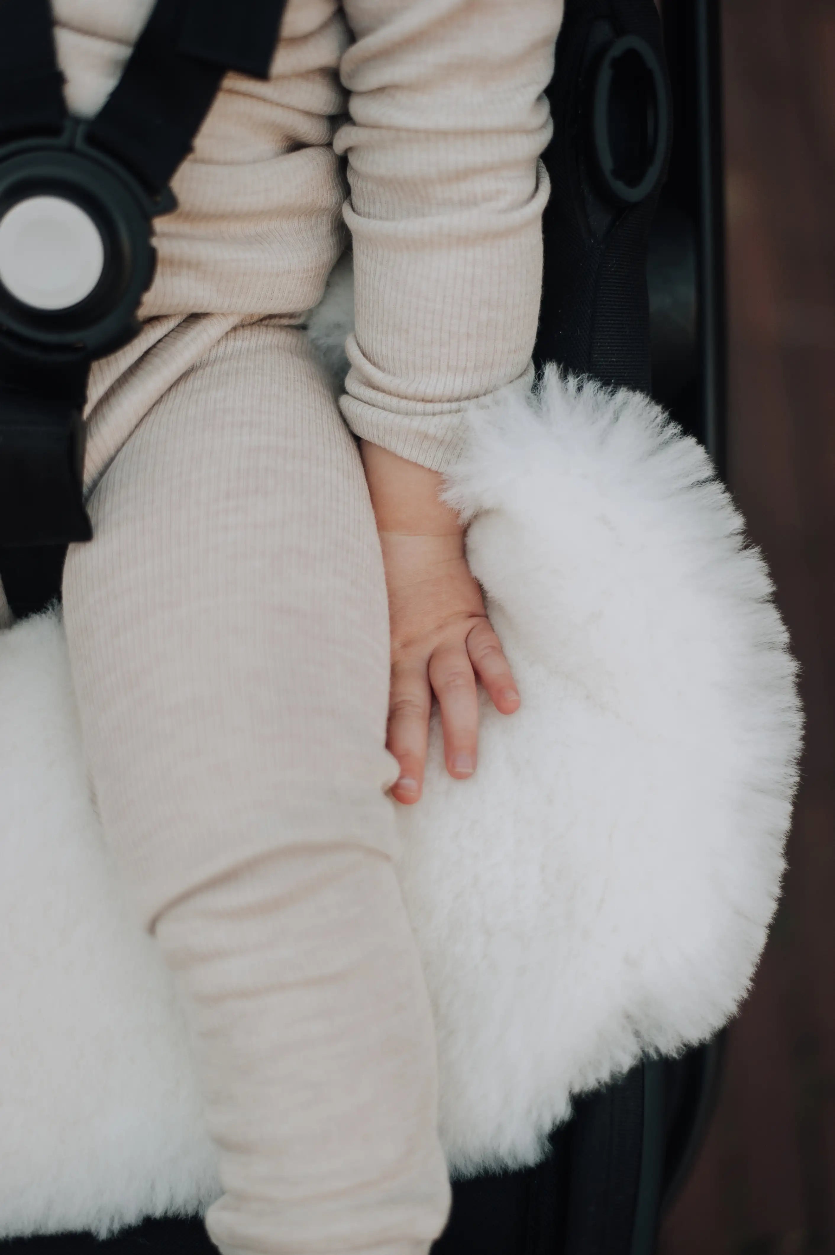 baby zittend in een kinderwagen met daarin een schapenvacht die hij vasthoudt met zijn hand